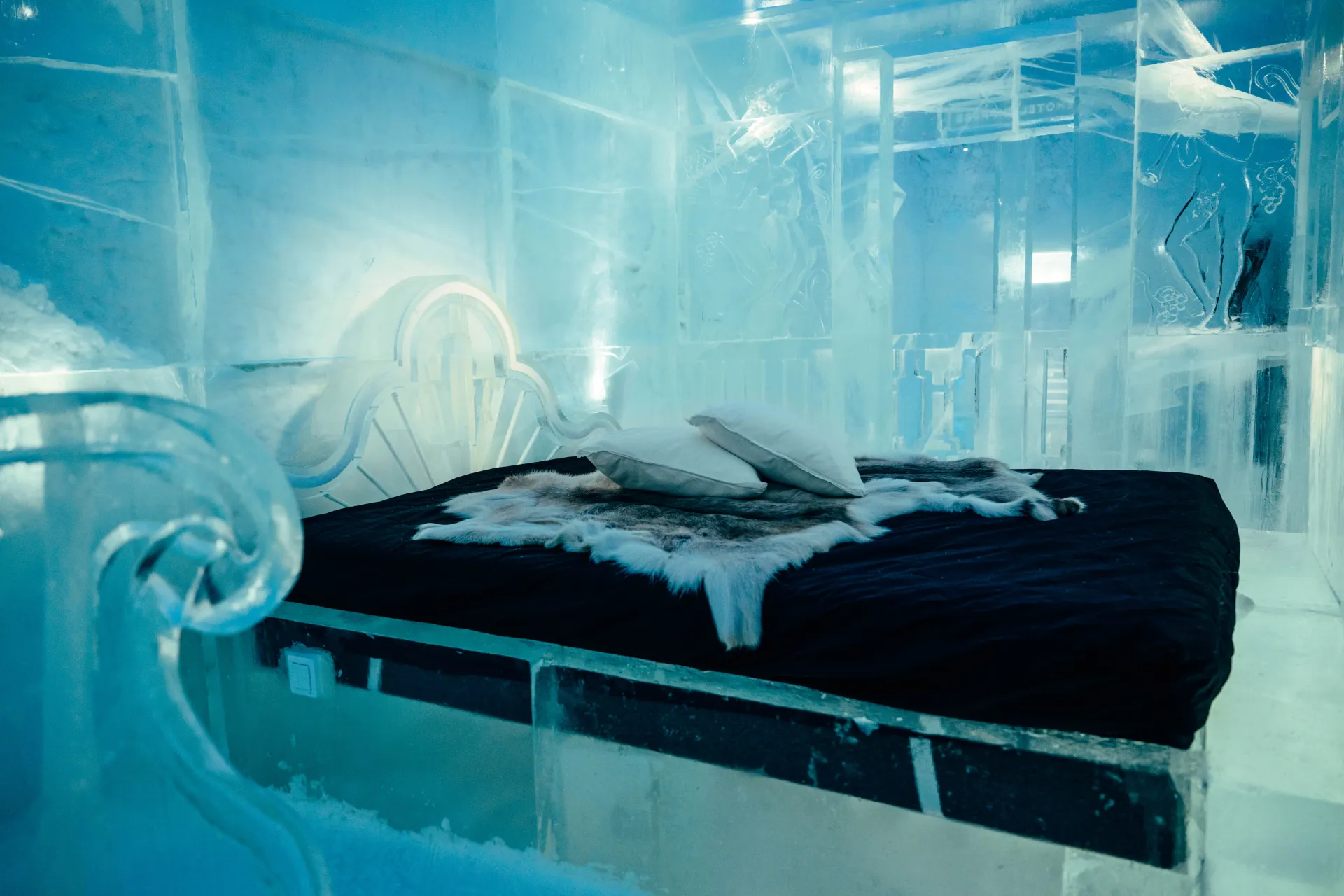 An ice-block bedroom with a carved headboard, a dark mattress and fur across the bed.